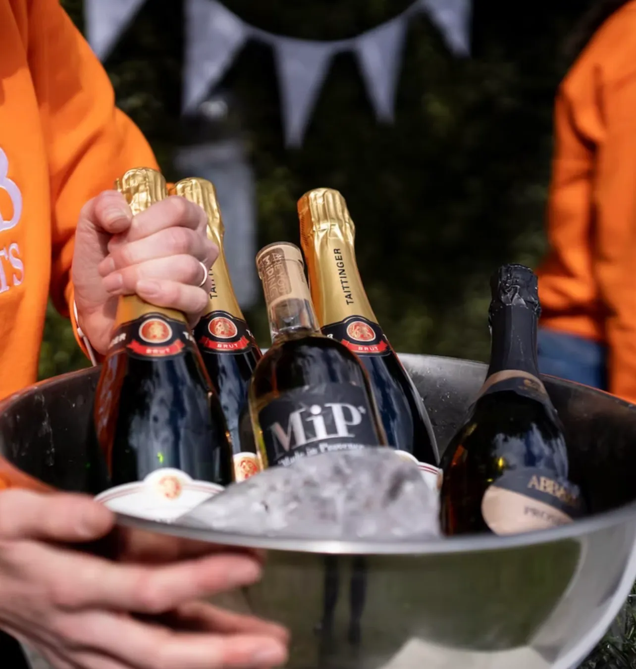 Bottles of champagne, prosecco and rosé packed into a steel bucket of ice, carried between two of the team