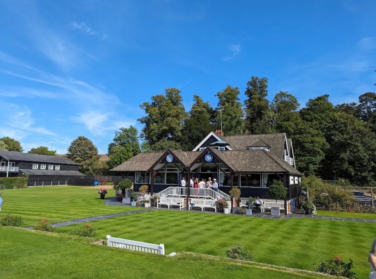 The clubhouse across the mown lawn on a summer afternoon, people gathered along the veranda
