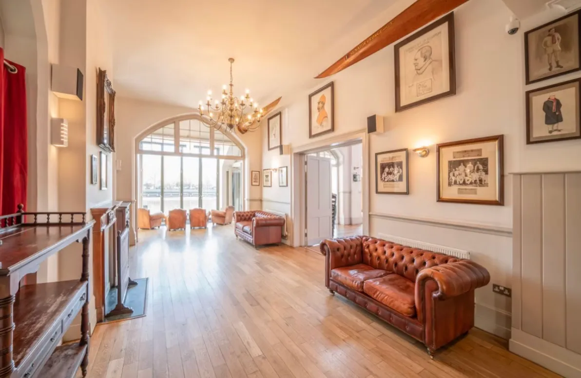 Leather sofas along a panelled room hung with framed crews and portraits, arched doors at the far end