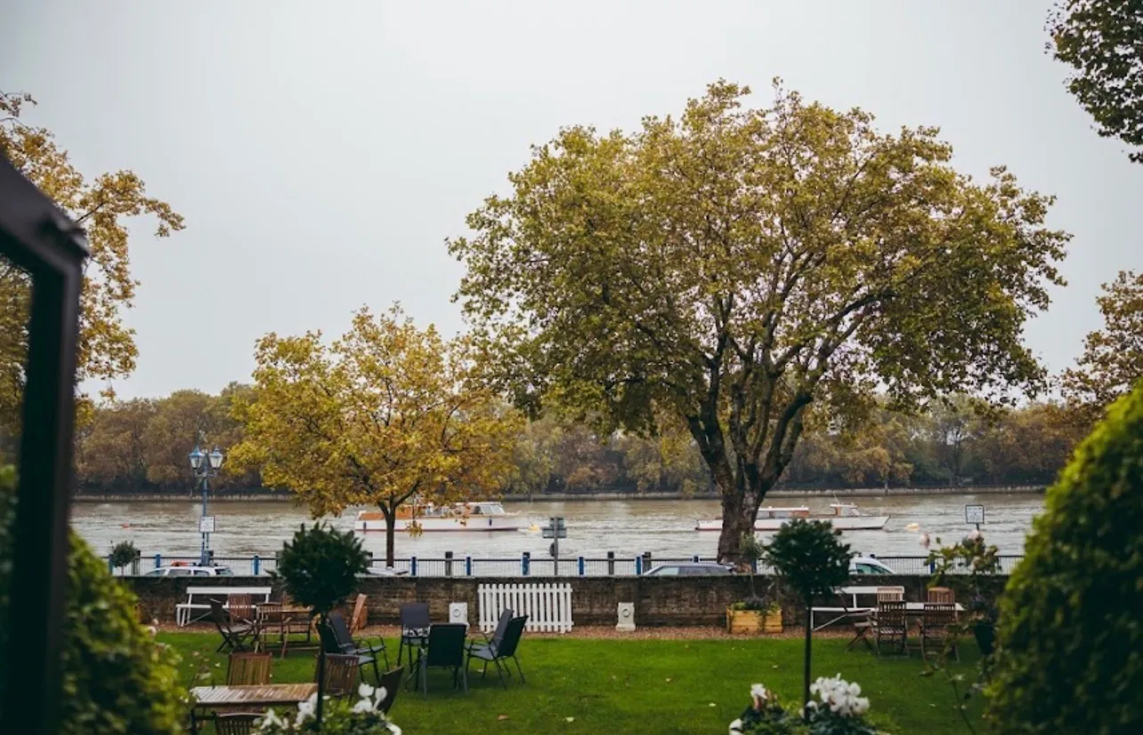 Garden tables and chairs on the lawn, with the river and the far bank beyond the wall